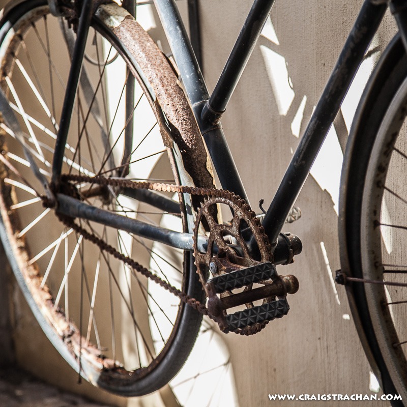 An old single-speed bicyle with rusty chain and rusty rear fender.
