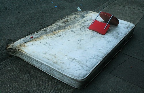 A dirty discarded mattress with a broken chair laying on top of it.