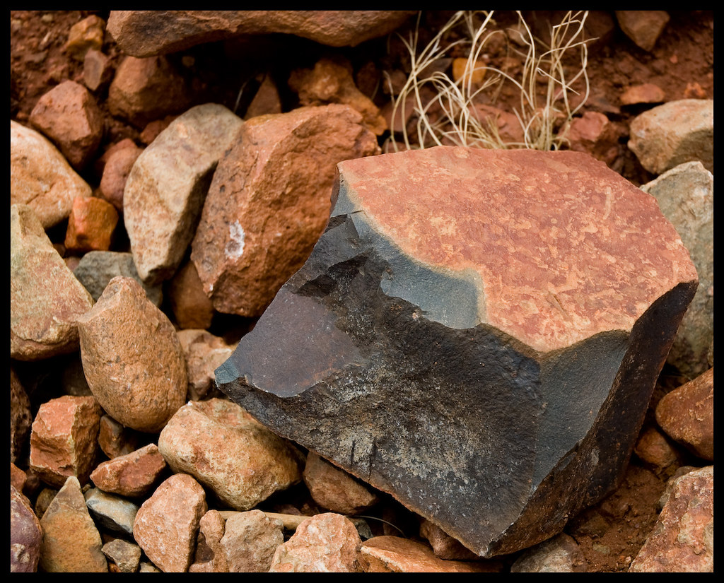 A lone red and slate-colored stone on a bed of reddish-brown rounded stones.